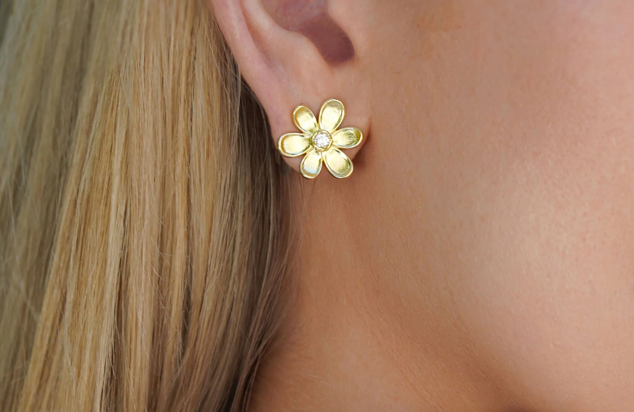 woman wearing a gold flower earring with diamond center