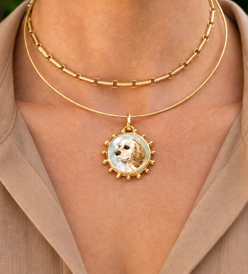 A close-up of a person's neck wearing a double-layered gold necklace with a custom oval pendant featuring a dog portrait.