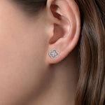 A close-up of a woman's ear wearing a 14K white gold clover-shaped stud earring with clear diamonds.