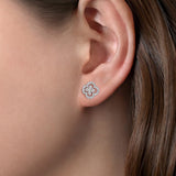 A close-up of a woman's ear wearing a 14K white gold clover-shaped stud earring with clear diamonds.