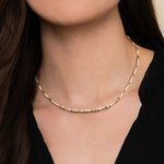 A close-up of a model's neck and chest wearing a delicate 14K yellow gold chain necklace with small clear diamond accents between each link.