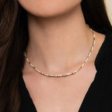 A close-up of a model's neck and chest wearing a delicate 14K yellow gold chain necklace with small clear diamond accents between each link.
