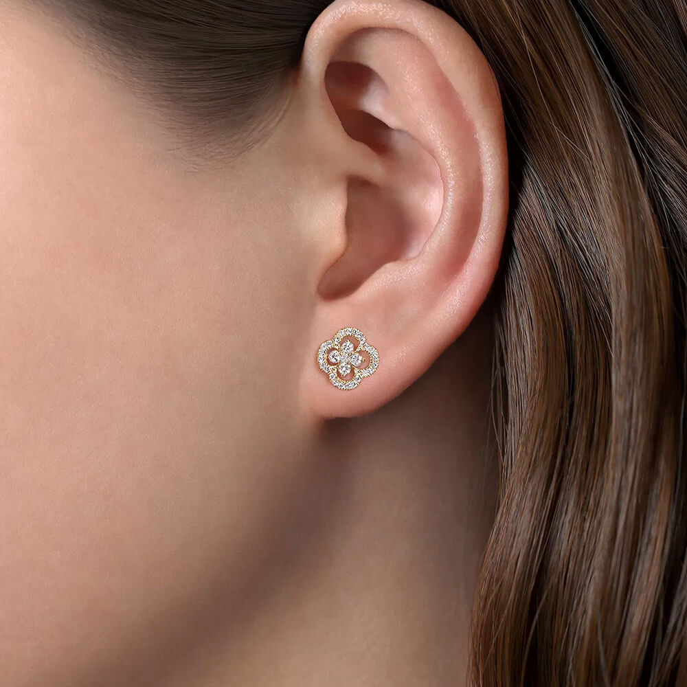 A close-up of a model's ear wearing a clover cutout stud earring in 14K yellow gold with diamonds. 