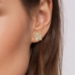 A close-up of a model's ear wearing a 14K yellow gold flower-shaped stud earring set with clear diamonds.