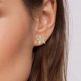 A close-up of a model's ear wearing a 14K yellow gold flower-shaped stud earring set with clear diamonds.