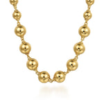 A gold beaded necklace with large, polished spherical beads connected by delicate chain links, shown on a clean white background.