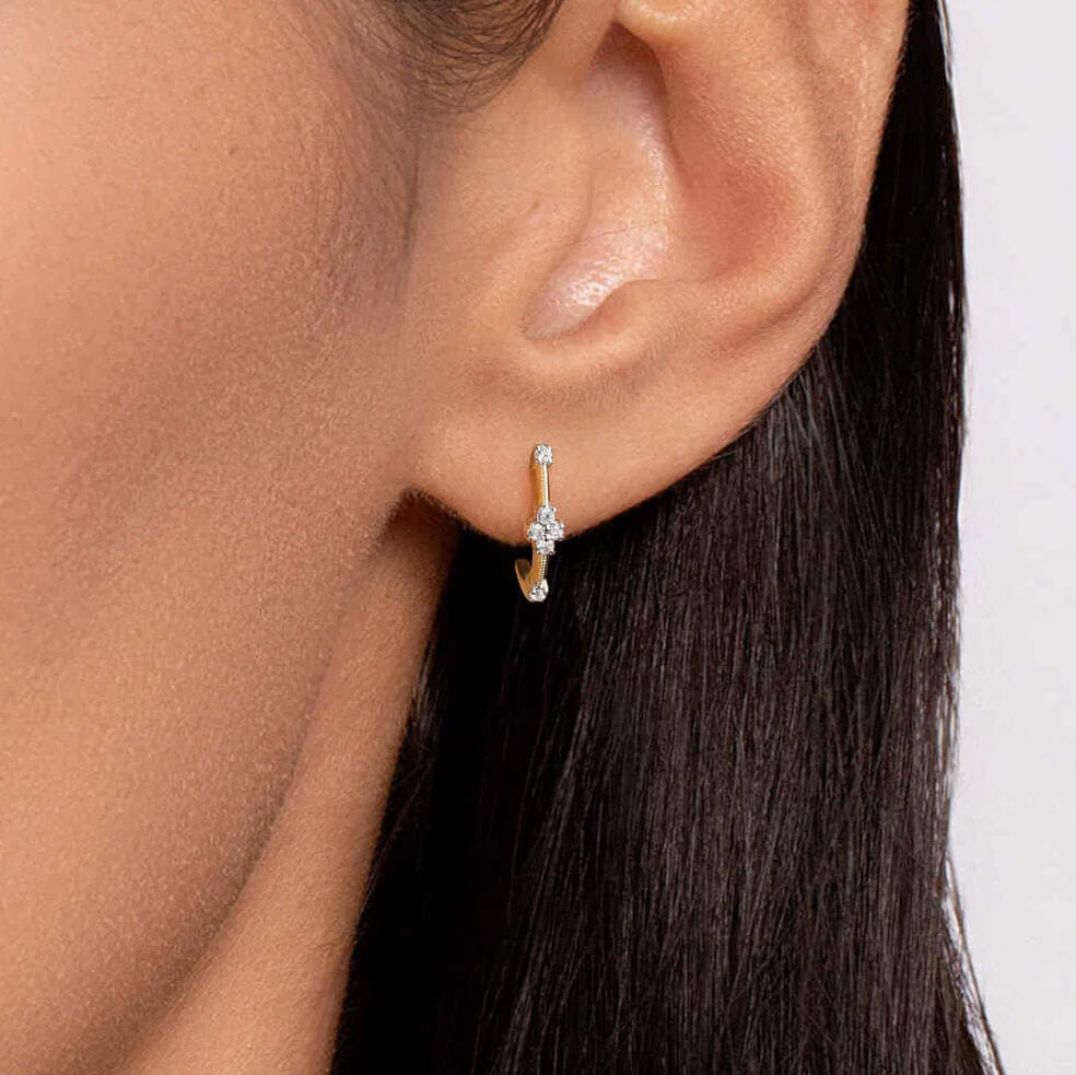 A close-up of a model's ear wearing a delicate 14K yellow gold J hoop earring with white sapphires