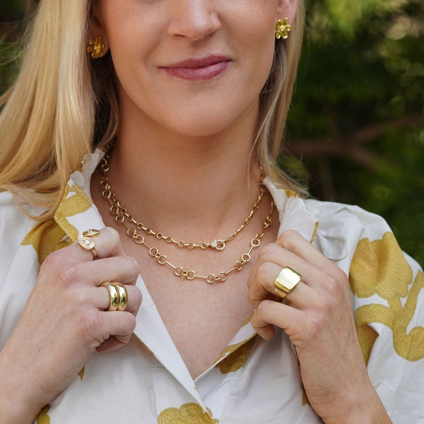 Woman wearing 14K gold jewelry outdoors with greenery in the background