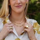 Woman wearing 14K gold jewelry outdoors with greenery in the background