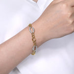 A 14K gold chain bracelet with two oval links set with small clear diamonds, worn on a woman's wrist against a white shirt background.