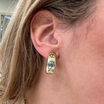 Close-up of an ear wearing a gold earring with blue topaz gemstones.