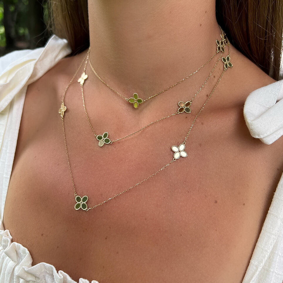 A close-up of a woman's neck wearing a layered gold necklace with small clover-shaped charms.