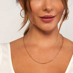 A close-up of a woman wearing a delicate elongated link chain necklace in a warm 14k yellow gold, wearing a white top against a clean white background.
