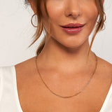 A close-up of a woman wearing a delicate elongated link chain necklace in a warm 14k yellow gold, wearing a white top against a clean white background.
