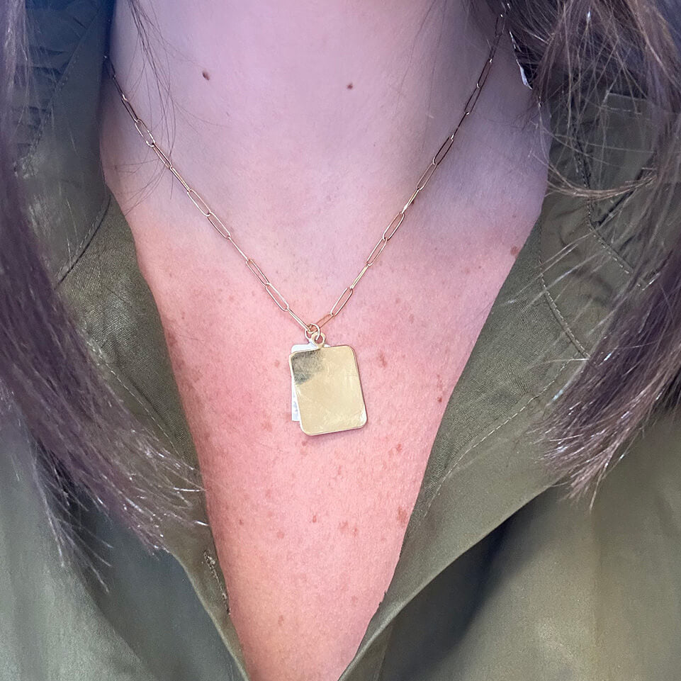 Gold necklace with a rectangular 14K yellow gold pendant on a woman wearing a green jacket.