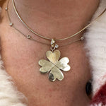 A close-up of a woman's neck wearing a layered gold necklace set. The set features a delicate chain with tiny clear diamonds and a larger chain with a 14K yellow gold clover pendant where the top leaf is a textured heart.