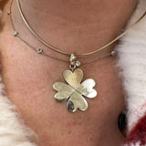 A close-up of a woman's neck wearing a layered gold necklace set. The set features a delicate chain with tiny clear diamonds and a larger chain with a 14K yellow gold clover pendant where the top leaf is a textured heart.