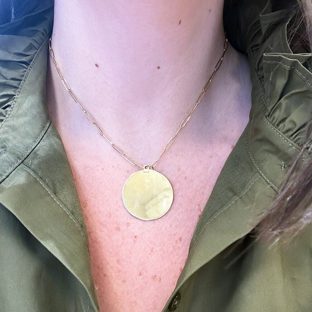 A close-up of a woman wearing a delicate gold chain necklace with a round, 14K gold gold pendant, styled with an olive green shirt.