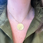 A close-up of a woman wearing a delicate gold chain necklace with a round, 14K gold gold pendant, styled with an olive green shirt.