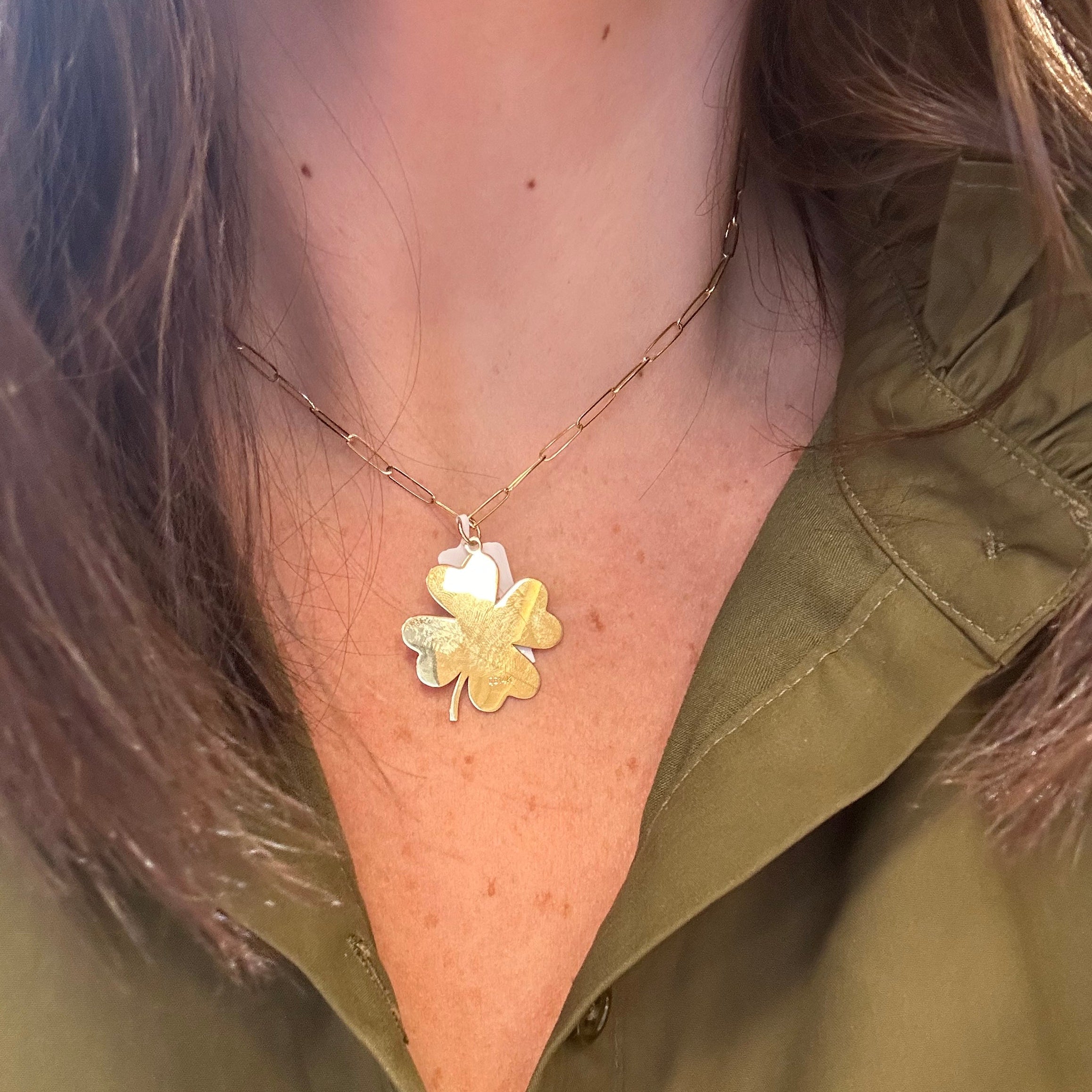 Close-up of a woman wearing a delicate necklace with a four leaf clover  pendant.