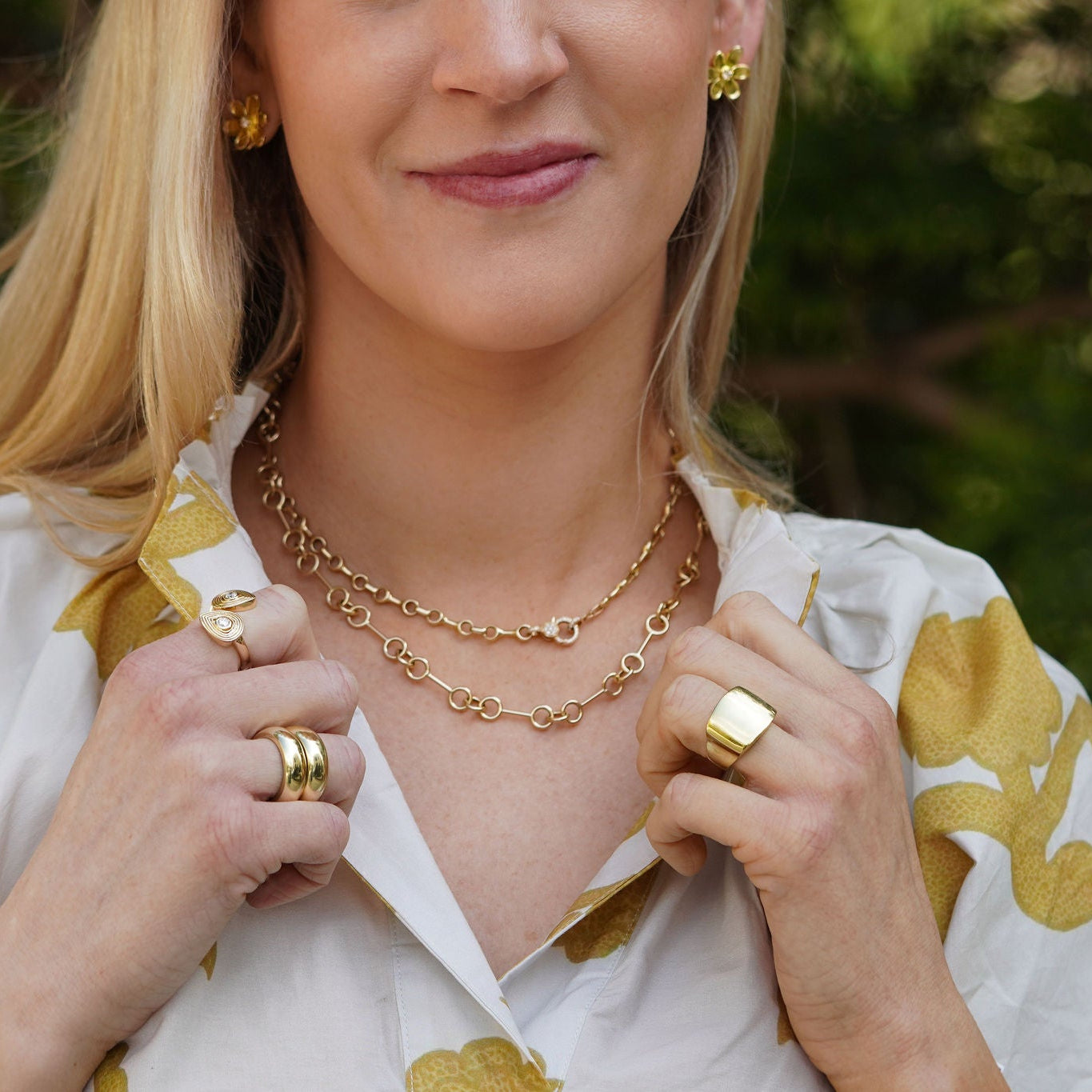 Woman wearing 14K yellow gold jewelry outdoors with greenery in the background