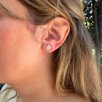 A close-up side view of a woman's ear wearing a 14K yellow gold diamond flower-shaped stud earring.