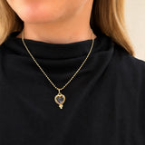 A close-up of a model wearing a delicate 14K yellow gold bead chain necklace with a heart-shaped pendant containing a dark, textured center and a small clear stone below it.