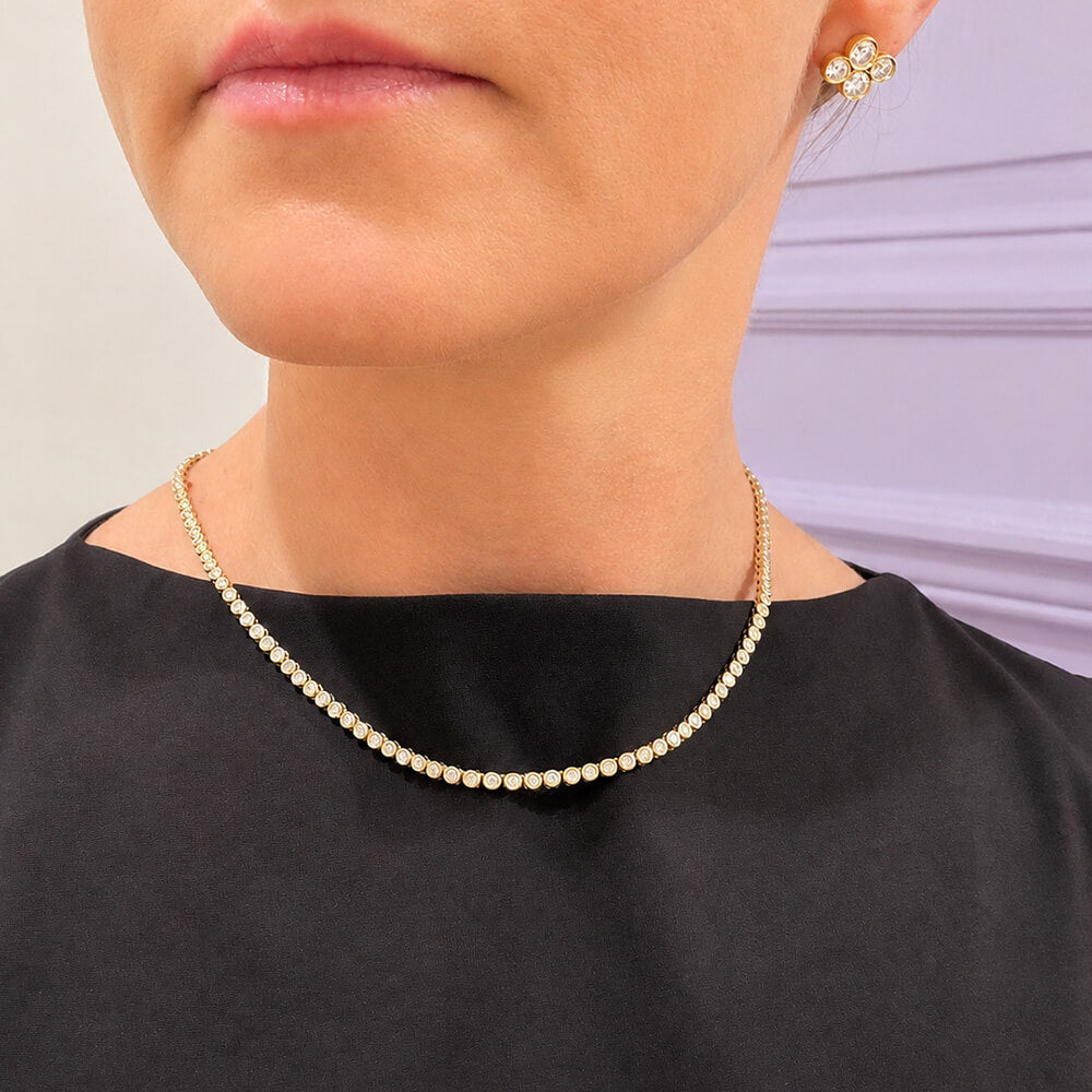 A close-up of a model wearing a 14K yellow gold bezel diamond tennis necklace 