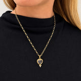 A gold heart pendant on a 14K yellow gold hollow oval chain necklace, worn by a model wearing a black turtleneck top.