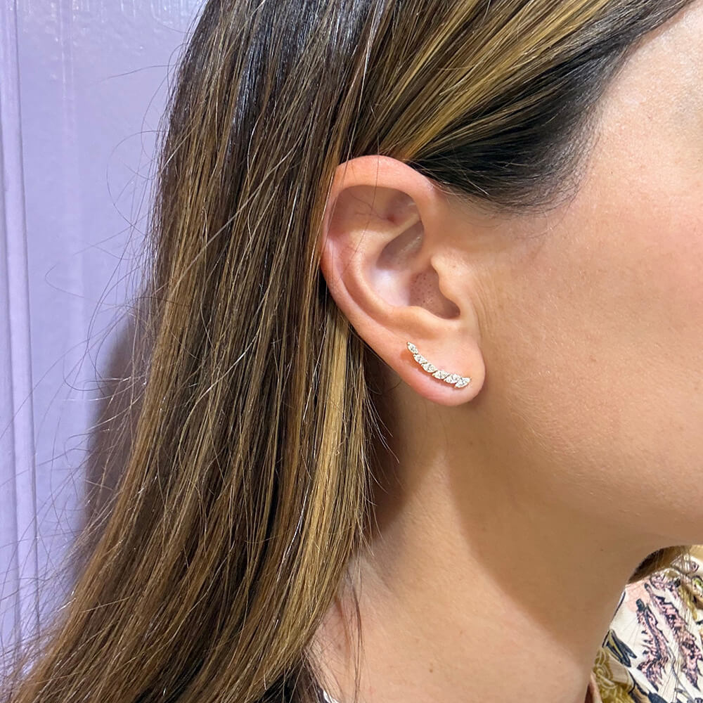 A close-up of a woman's ear wearing a small curved 14K yellow gold marquise-shaped diamond earring 