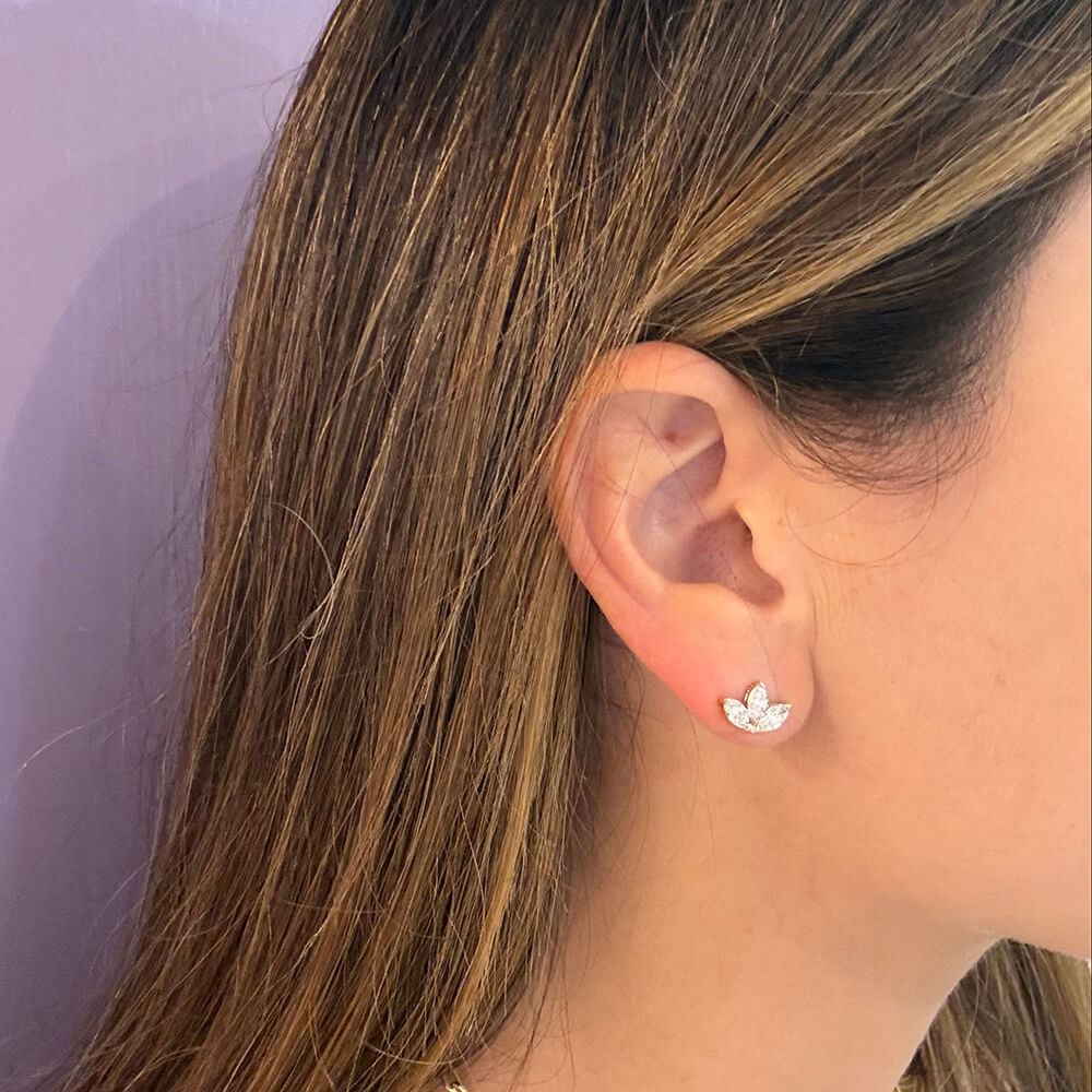 A close-up of a woman's ear wearing a small 14K yellow gold stud earring with three marquise diamonds arranged in a leaf or clover-like shape.