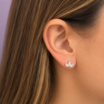A close-up of a woman's ear wearing a small 14K yellow gold stud earring with three marquise diamonds arranged in a leaf or clover-like shape.