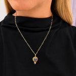 A 14K yellow gold chain necklace with a heart-shaped pendant featuring a dark blue-gray stone, worn by a model in a black turtleneck top.