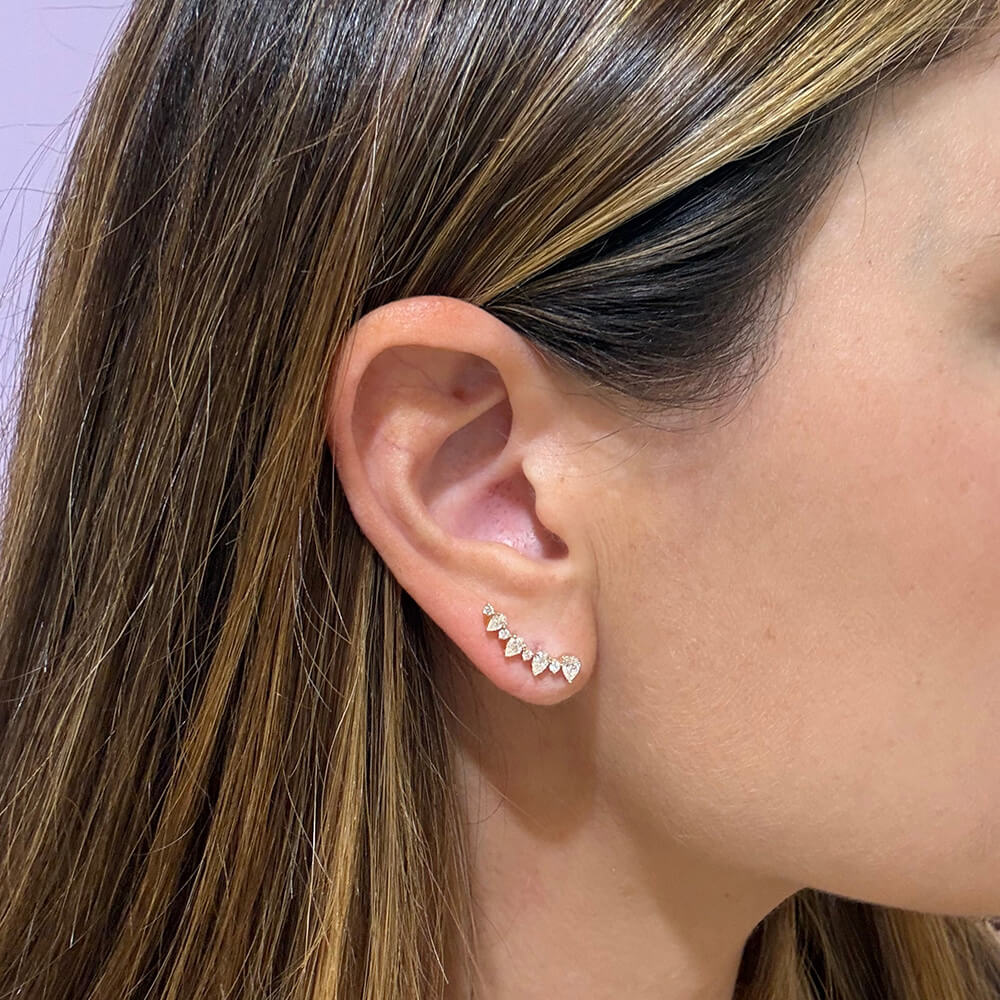 A close-up of a woman's ear wearing a 14K yellow gold earring with a small curved row of clear diamonds
