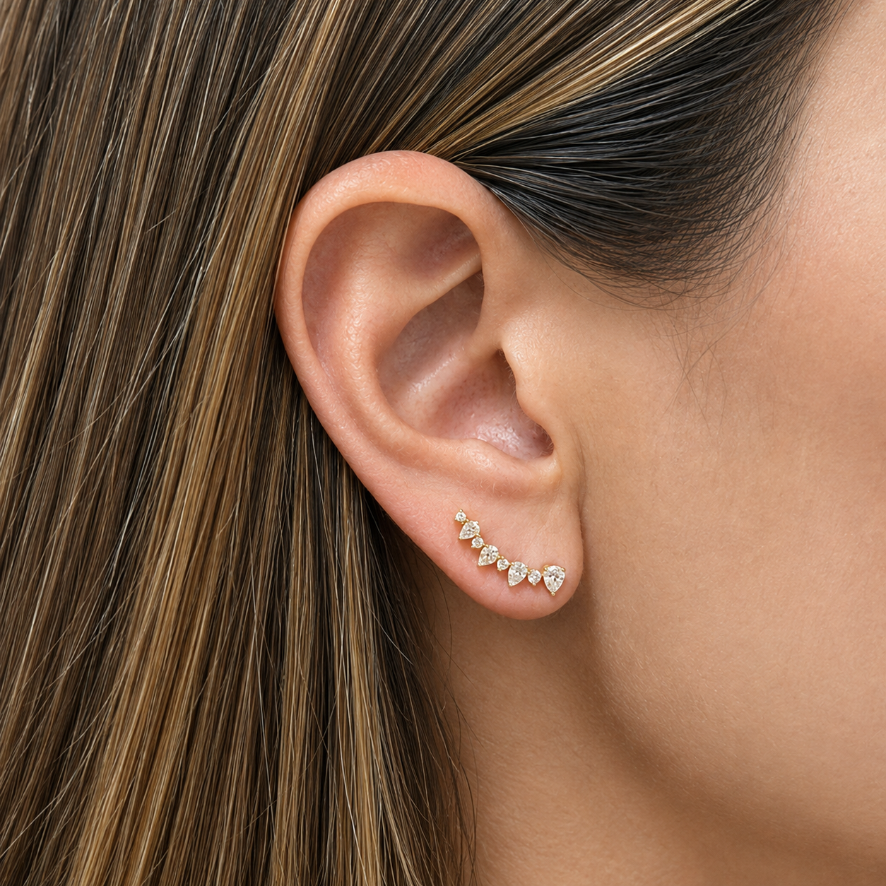 A close-up of a woman's ear wearing a 14K yellow gold earring with a small curved row of clear diamonds