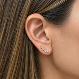 A close-up of a woman's ear wearing a 14K yellow gold earring with a small curved row of clear diamonds