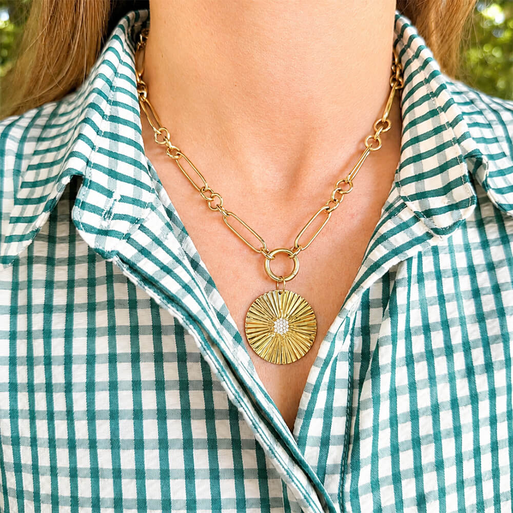 A gold chain necklace with a 14K gold fluted disc pendant with diamonds worn by a woman in a green and white checkered shirt.