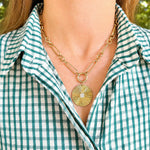 A gold chain necklace with a 14K gold fluted disc pendant with diamonds worn by a woman in a green and white checkered shirt.