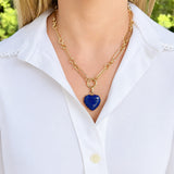 A gold chain necklace with a heart-shaped blue Lapis gemstone pendant, worn by a model wearing a white collared shirt.