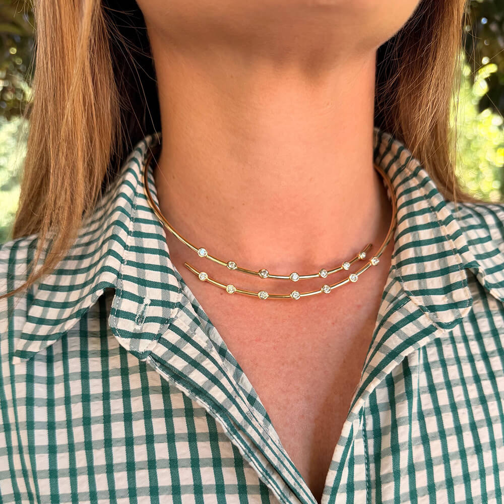 A close-up of a woman wearing a delicate double-layered 14K gold necklace with small bezel diamonds 