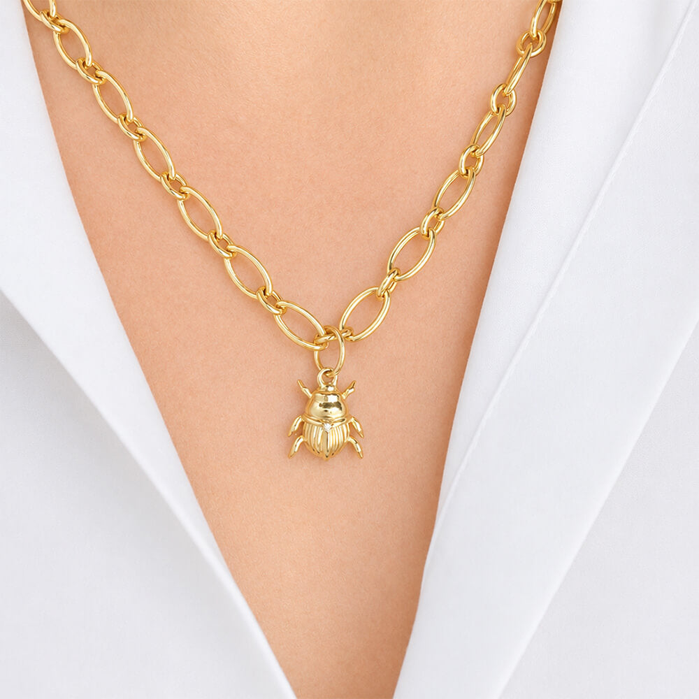 A gold chain necklace with a 14K gold beetle pendant, worn on a model's neck over a white collared shirt.