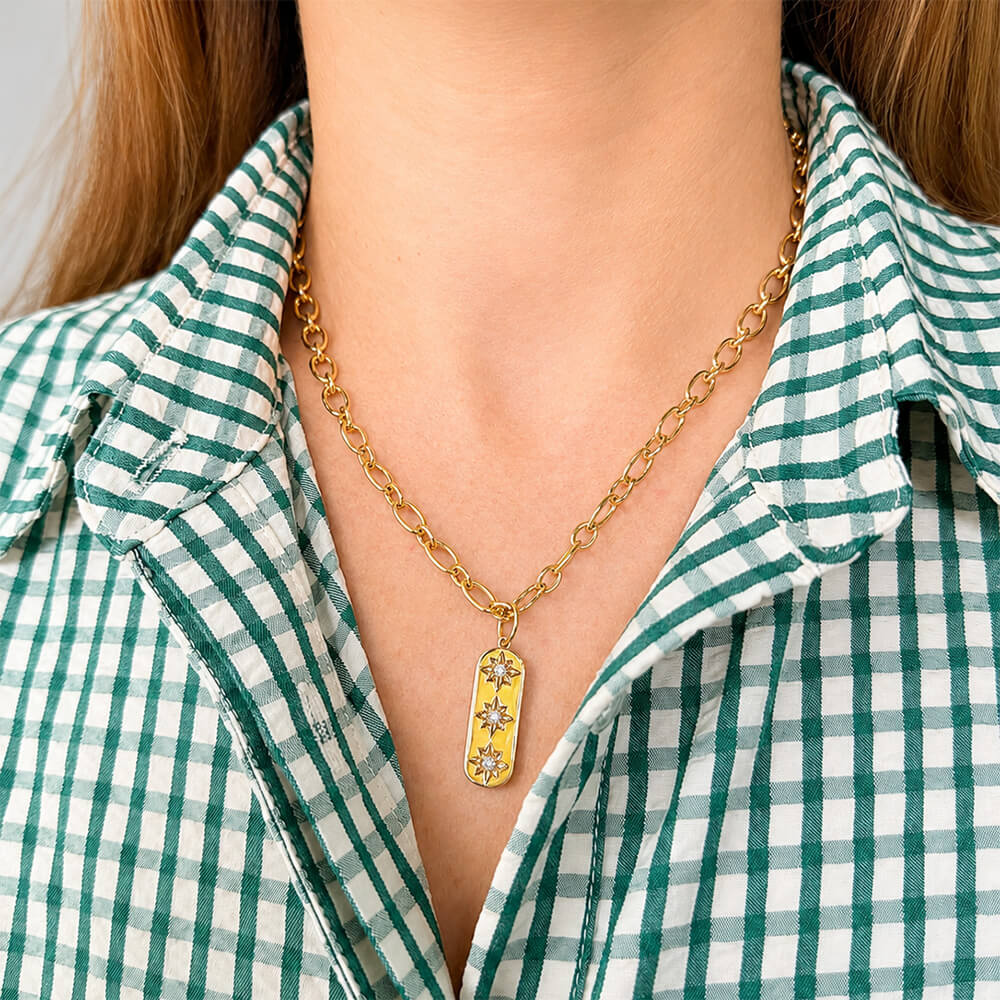 A gold chain necklace with a vertical 14K gold bar pendant featuring three diamond star-like accents, worn by a woman in a green and white checkered shirt.