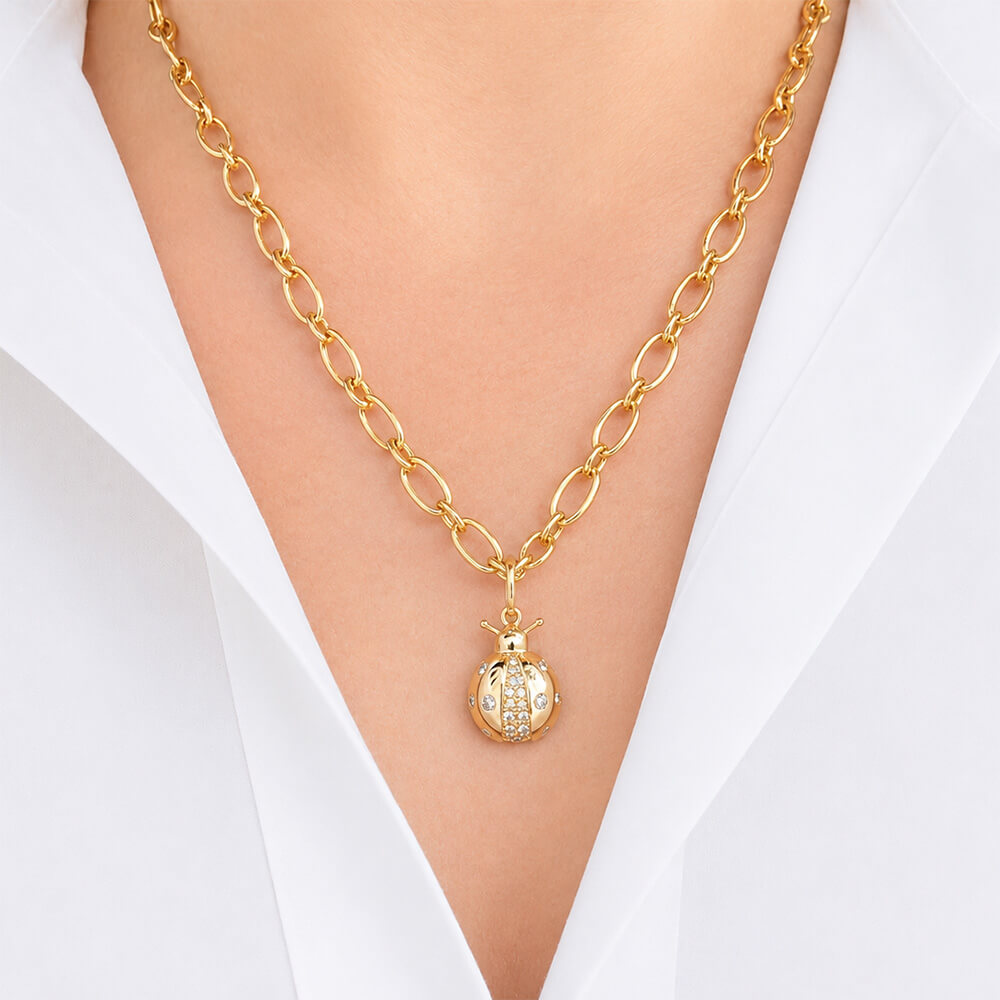 A gold chain necklace with a 14K gold ladybug pendant, worn on a model's neck over a white collared shirt. The pendant is detailed with small clear diamonds.