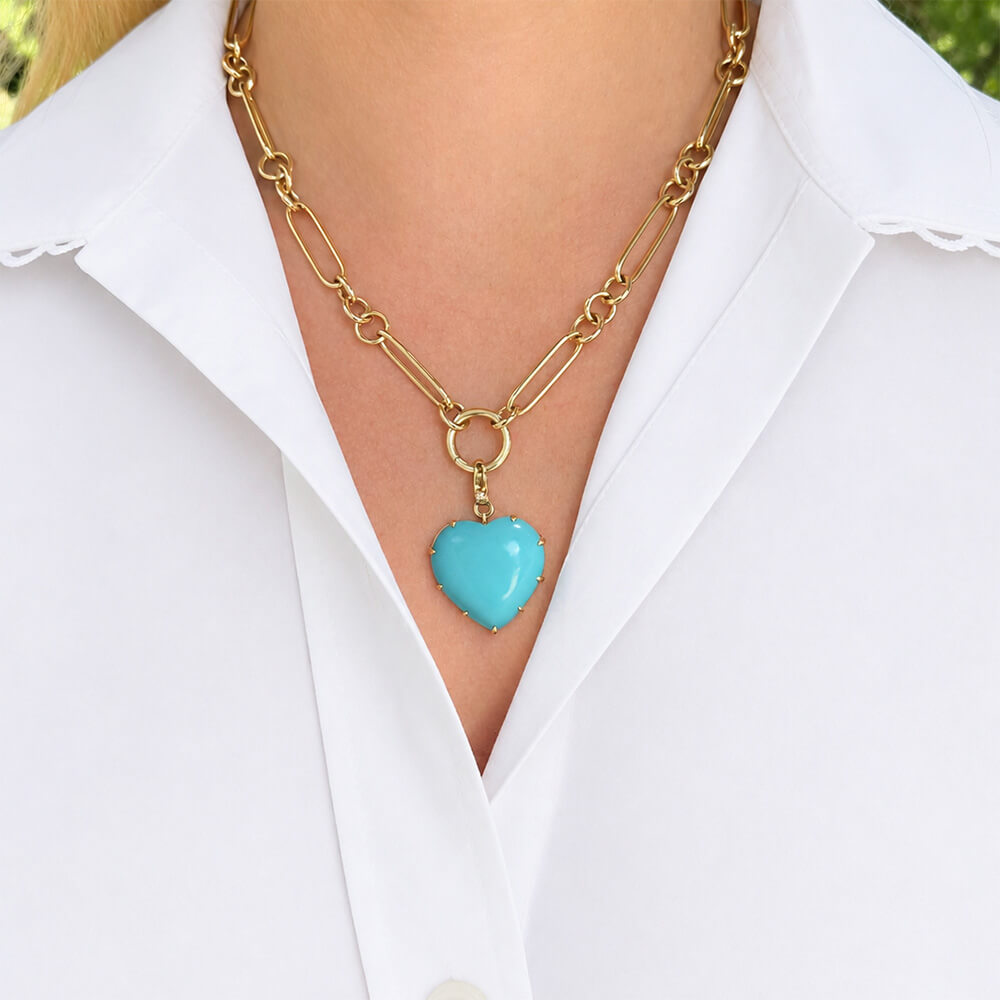 A gold chain necklace with a turquoise heart pendant, worn by a model in a white collared shirt.