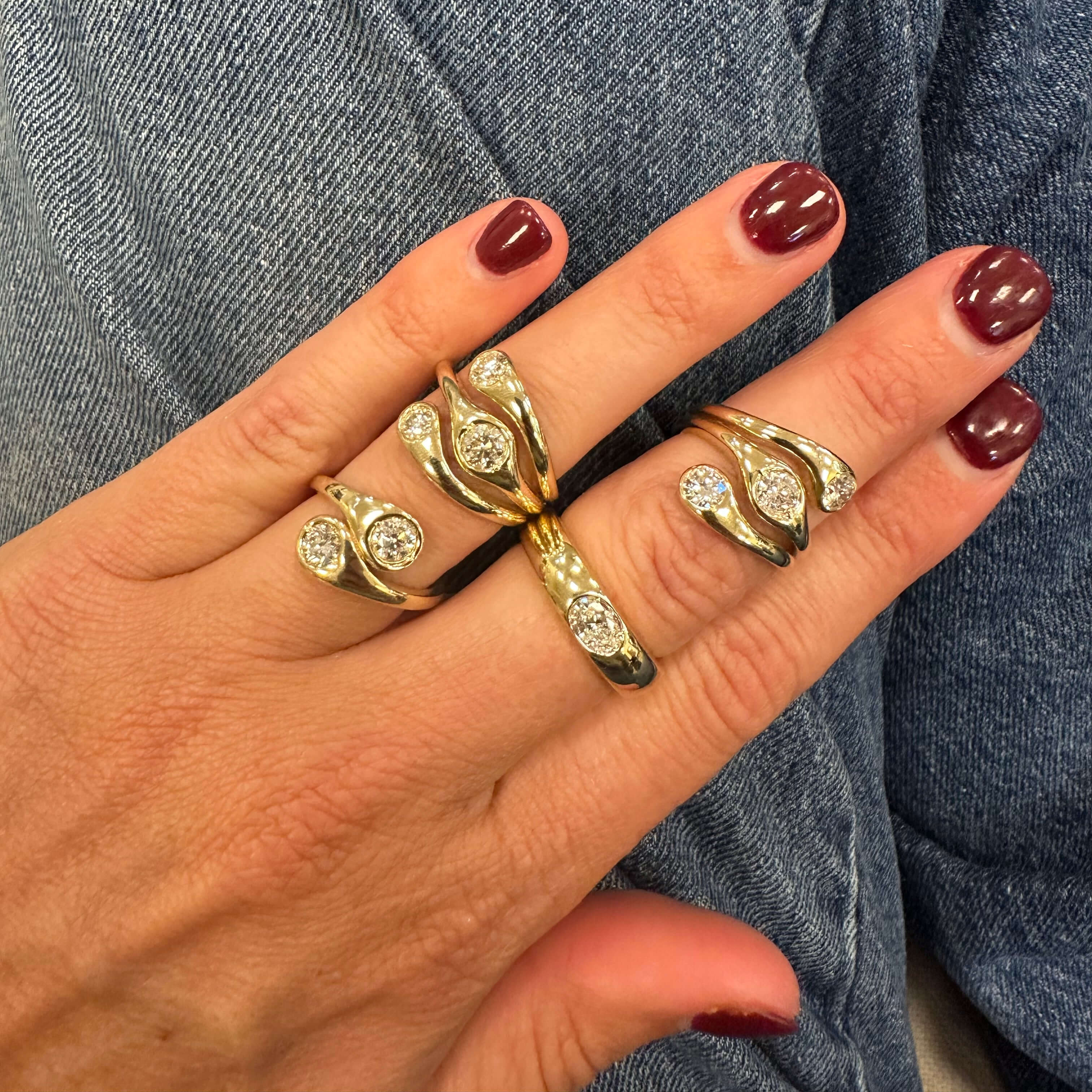 Hand wearing multiple gold rings with diamonds against a denim background
