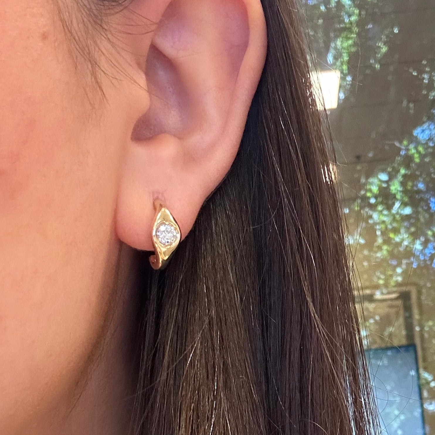Close-up of an ear with a diamond earring, hair partially covering the face.