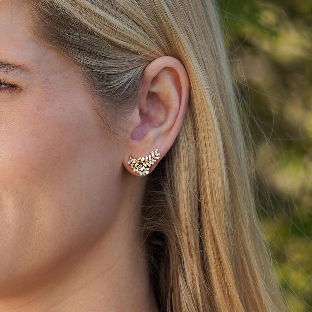 Close-up of a woman's ear wearing a 14K gold leaf shaped earring with diamonds 