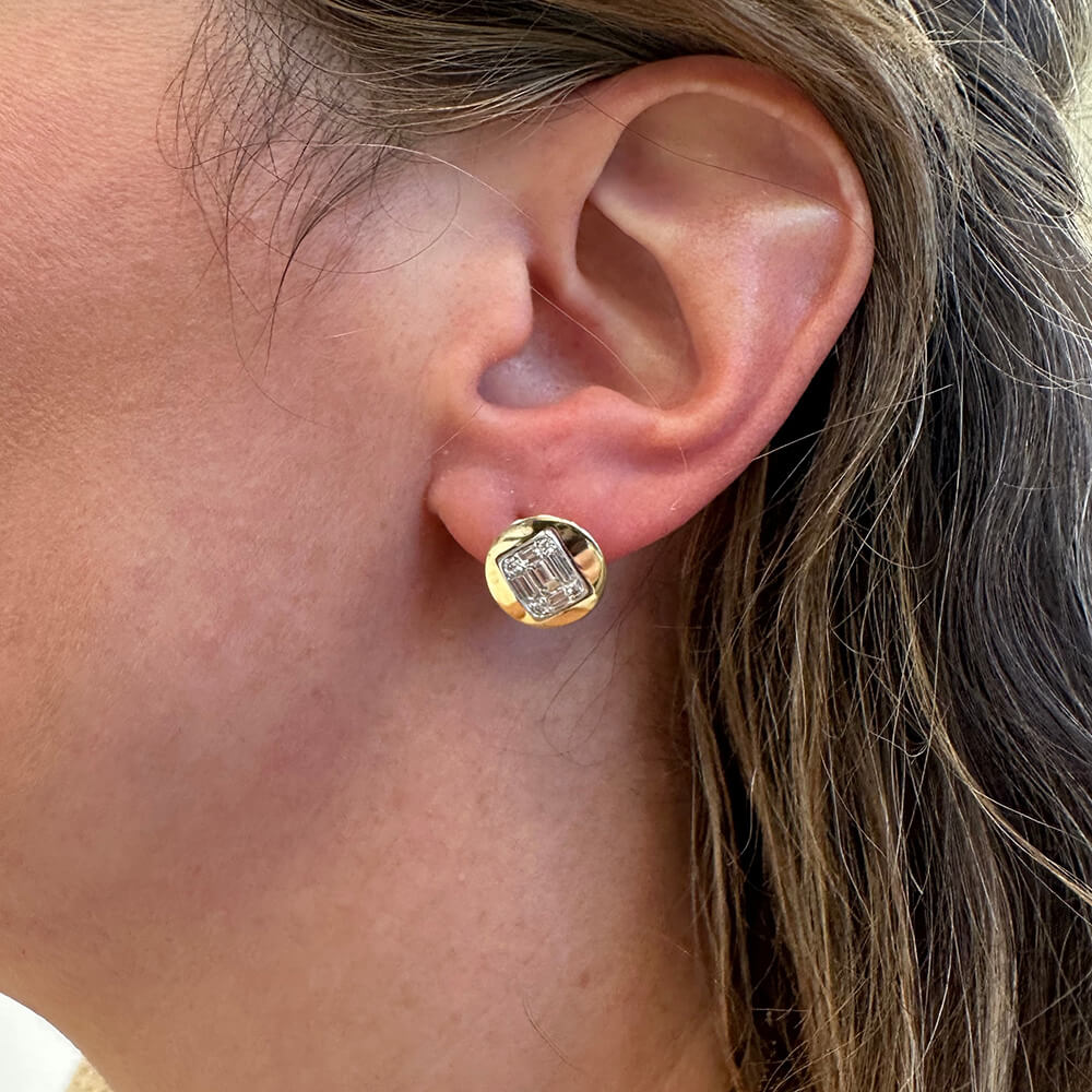 A close-up of a woman's ear wearing a 14k gold stud earring with a clear rectangular diamond.