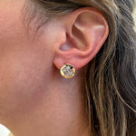A close-up of a woman's ear wearing a 14k gold stud earring with a clear rectangular diamond.