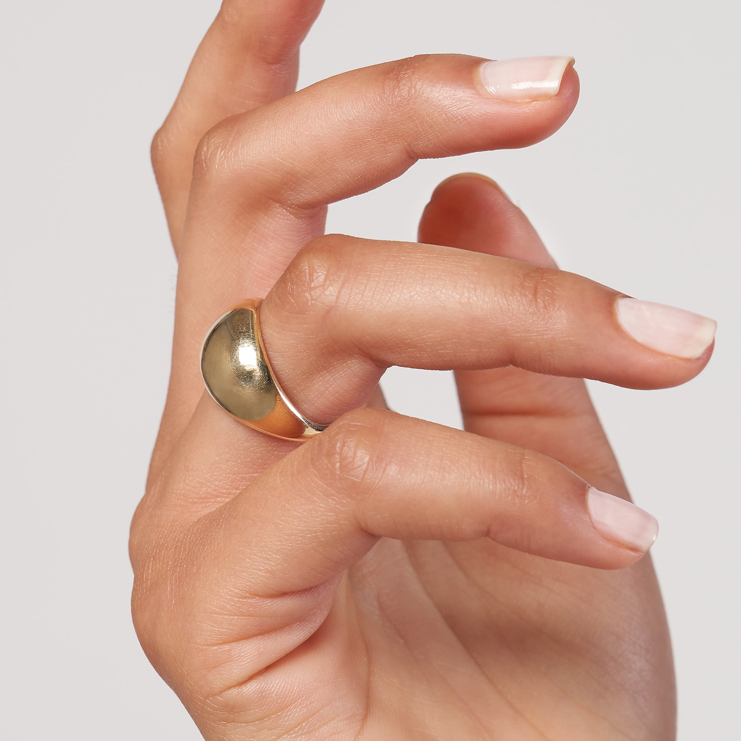 Hand wearing a 14K gold Dome ring on a plain background